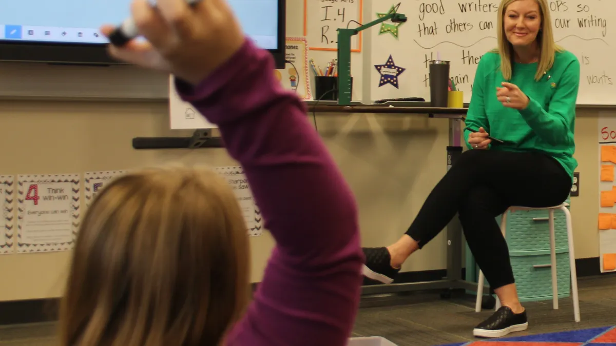 A female teacher points to a girl with her hand up in a classroom