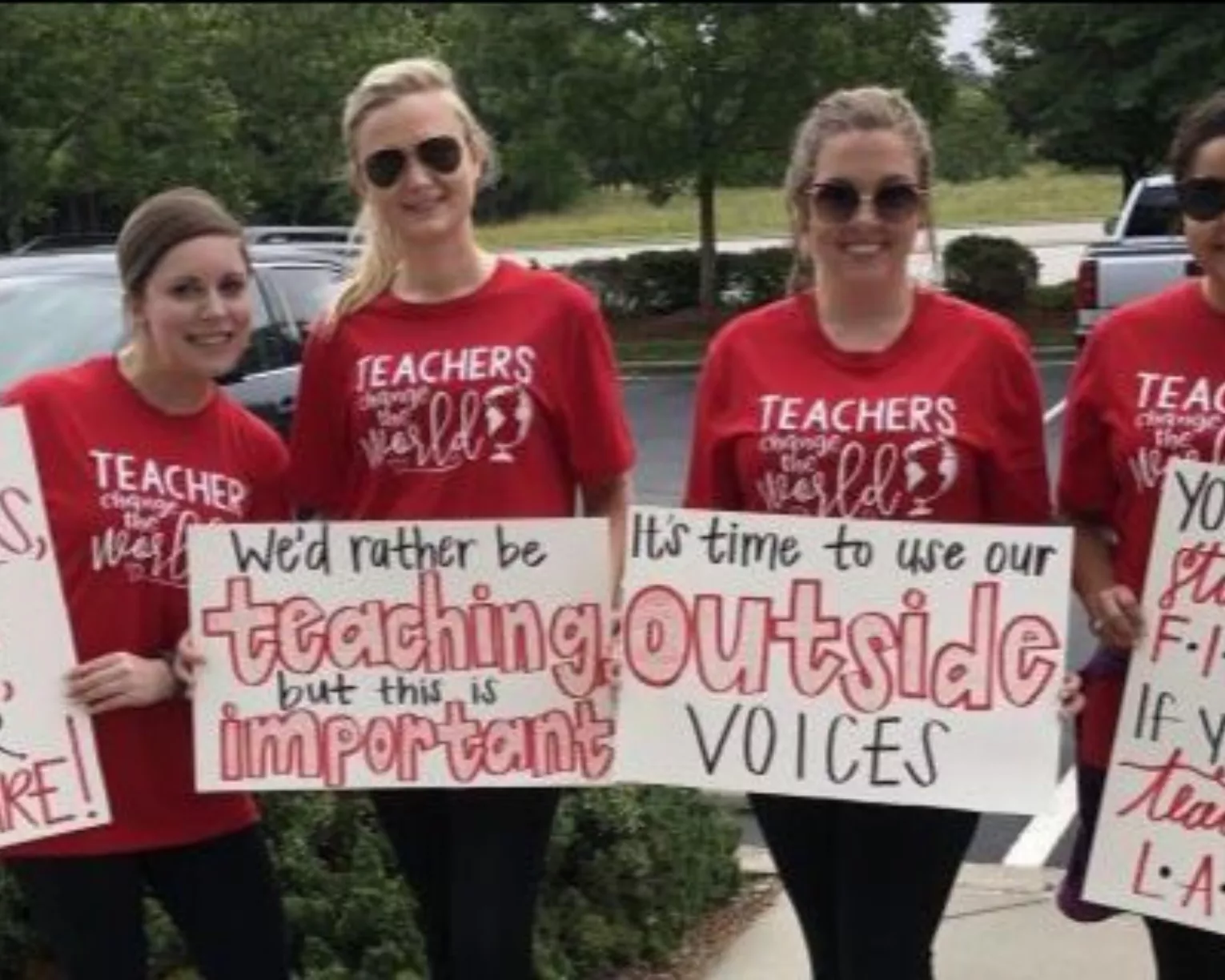 ISEA members pose with signs as they advocate for students. One says "We'd rather being teaching, but this is important." Another says, "It's time to use our outside voices."