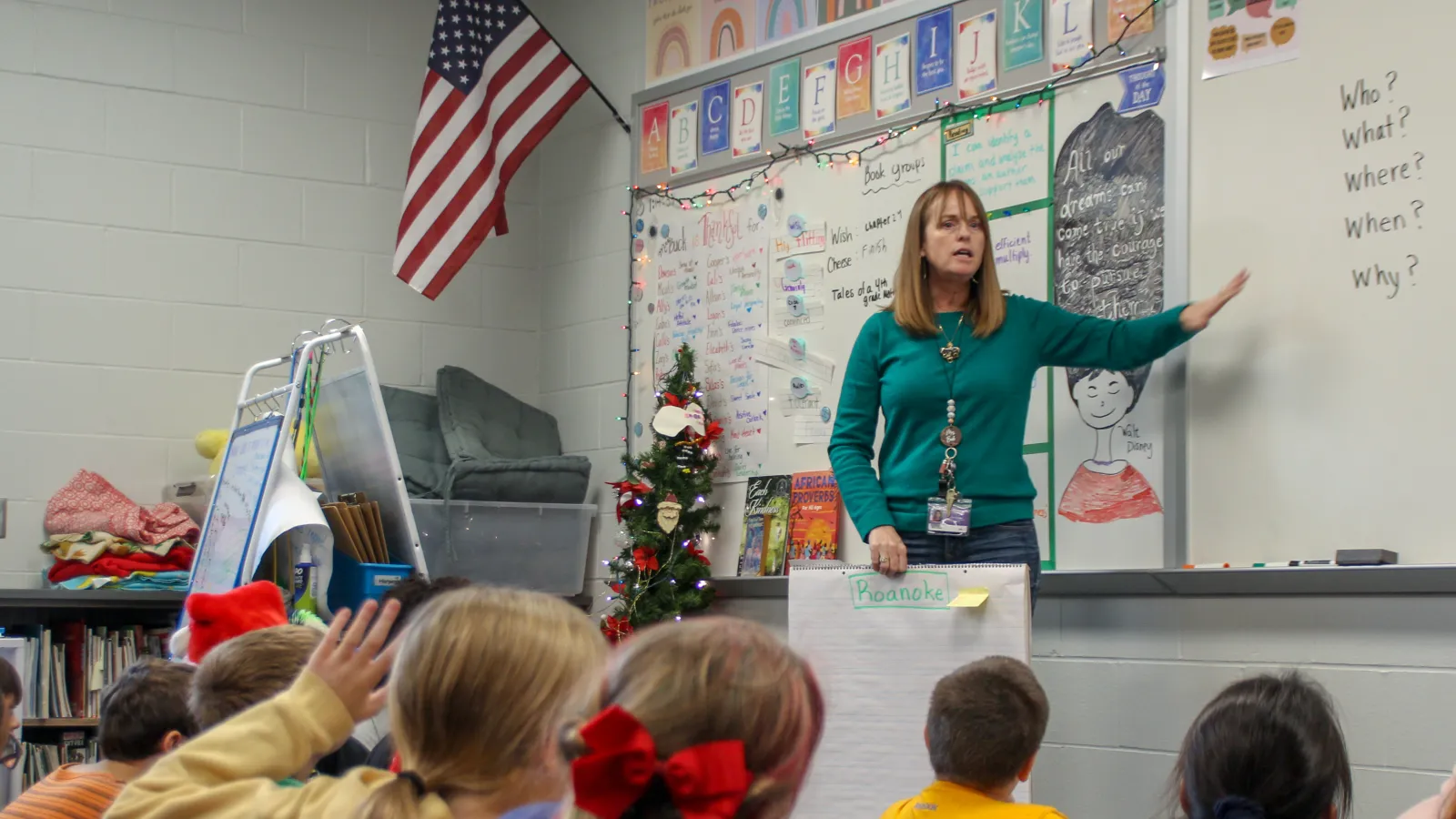 A female educator pointing to a whiteboard with children looking on