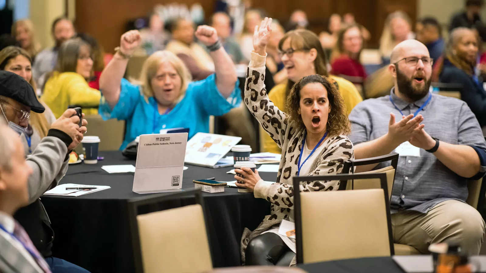 a group of teacher seated at a table cheering with arms raised