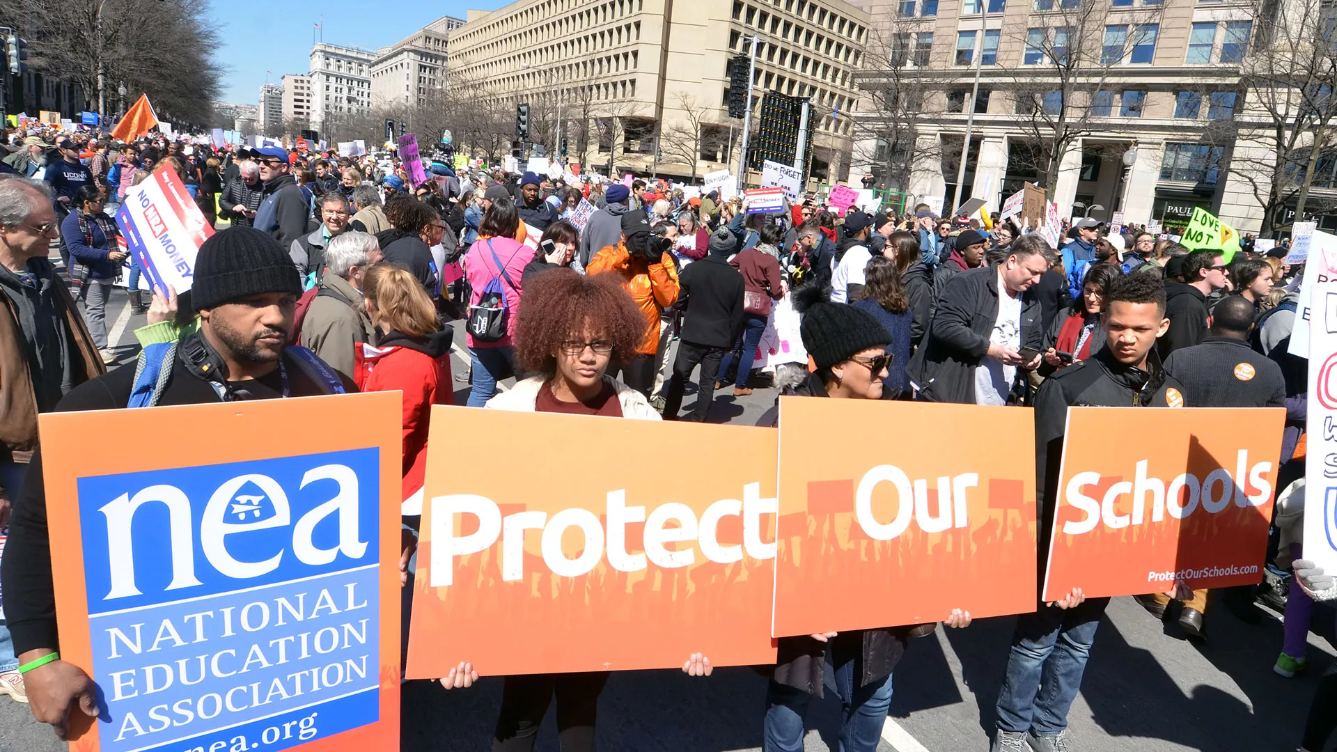 Educators hold up signs that read Protect Our Schools