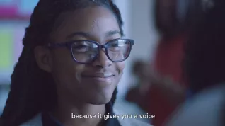 Black student with glasses smiles with subtitle "because it gives you a voice."