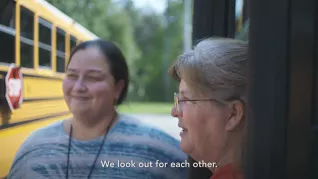 Two educators stand outside school bus with subtitle "we look out for each other."