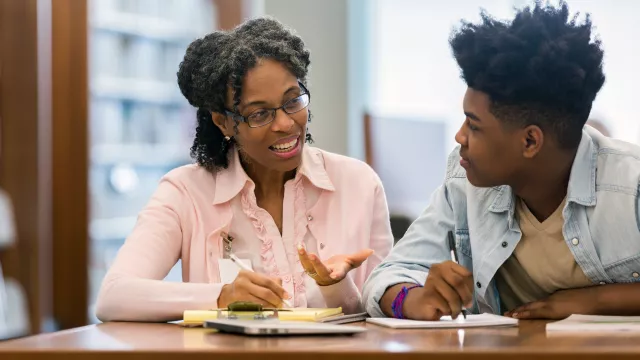 Black educator working with black teen in school library