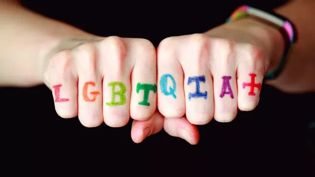A person with LGBTQIA+ written in rainbow colors across their knuckles