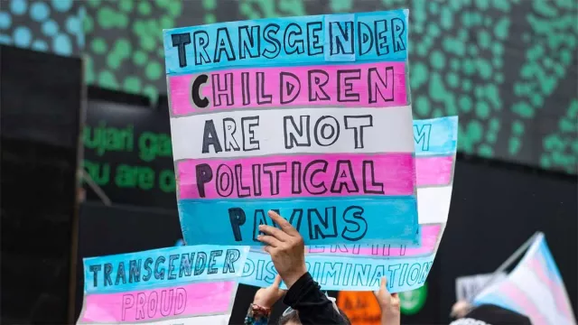 A woman holds a sign reading Trans Children Are Not Political Pawns